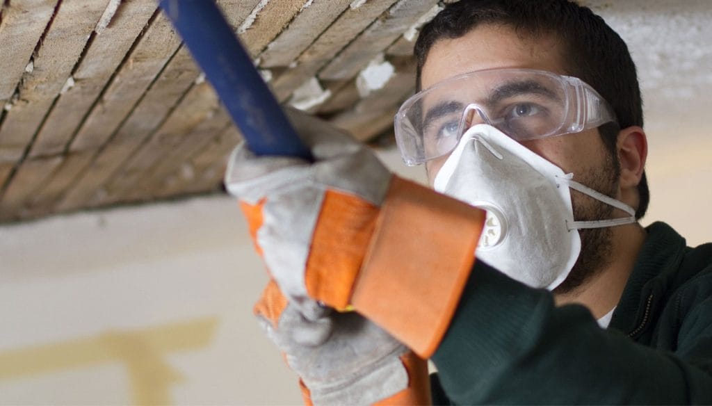 A professional with personal protective equipment removes ceiling water damage during water damage restoration in Logan, UT.